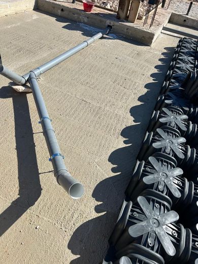 Tubi in PVC grigi rotti accanto a tappeti geogriglia in plastica nera su cemento.