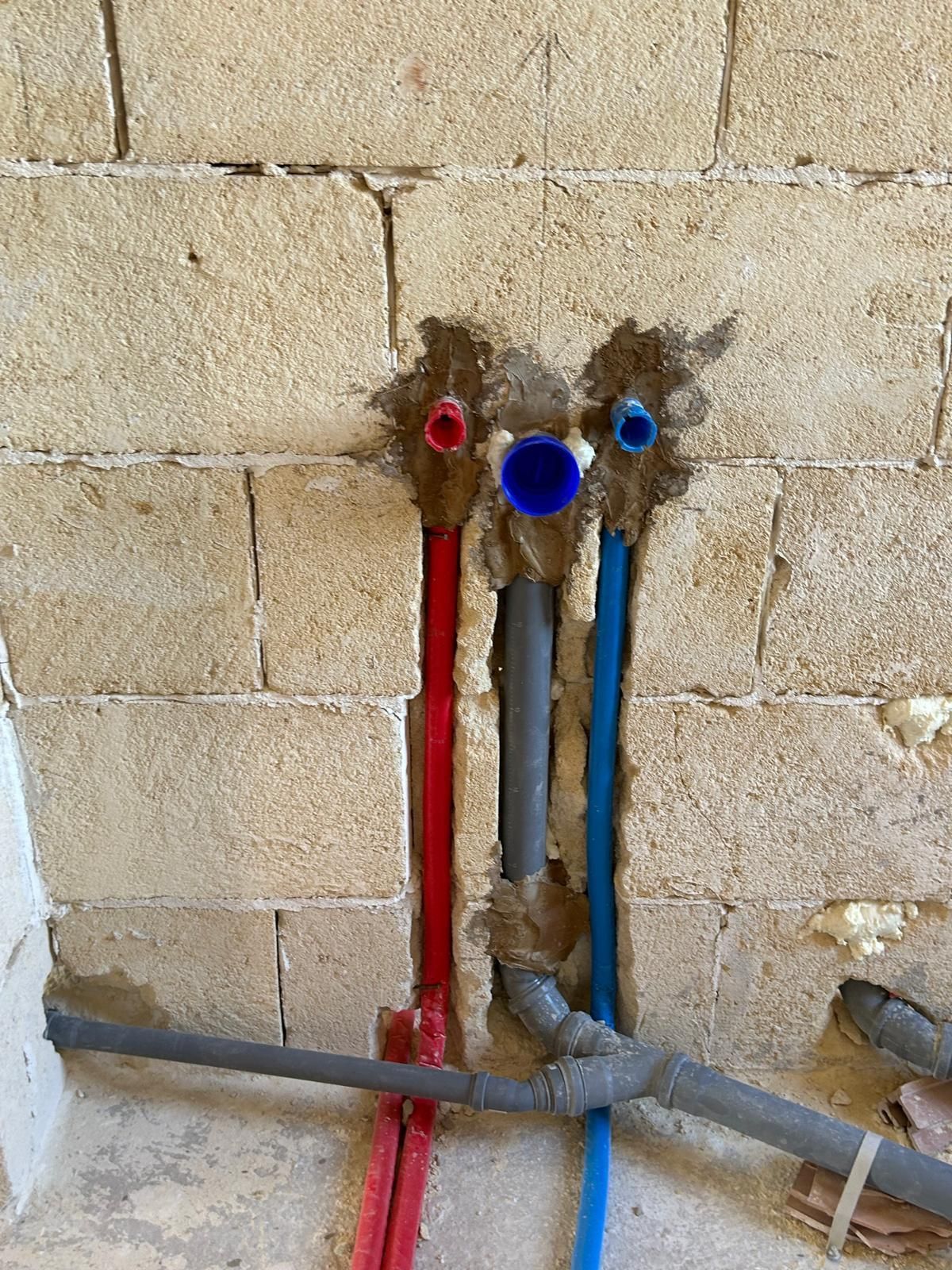 Tubature a vista rosse, blu e grigie incastonate in una parete beige grezza.