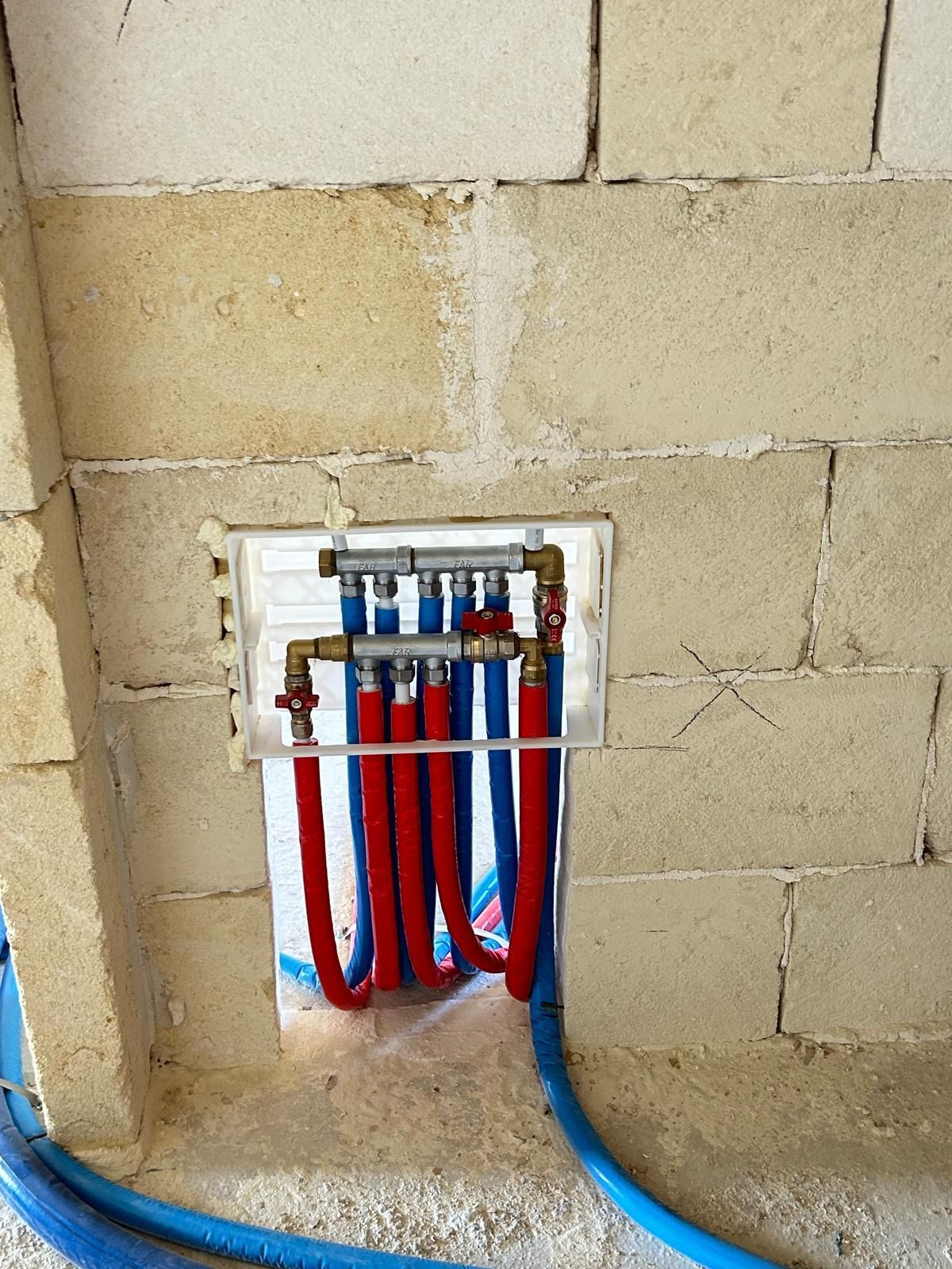 Collettore idraulico con tubi rossi e blu installato in un'apertura a muro.