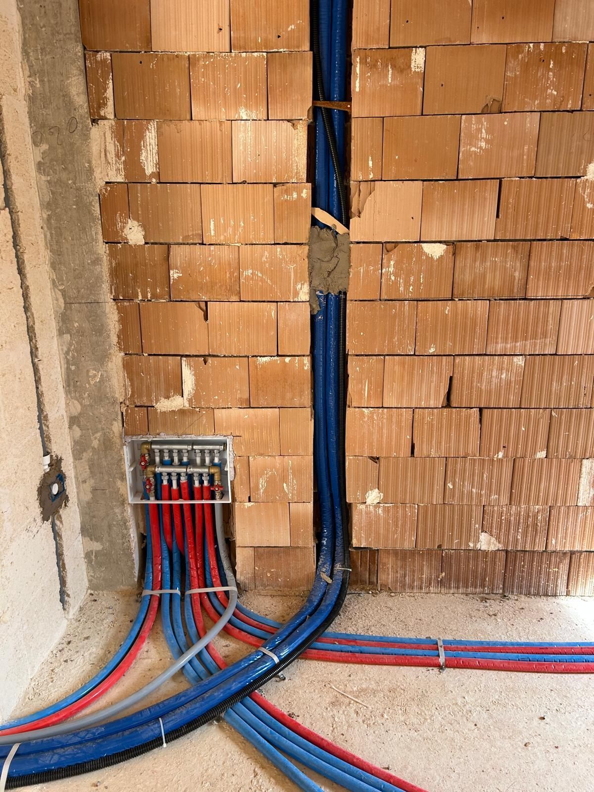Condotti e cavi elettrici blu e rossi in una cavità del muro con mattoni a vista e una scatola di derivazione