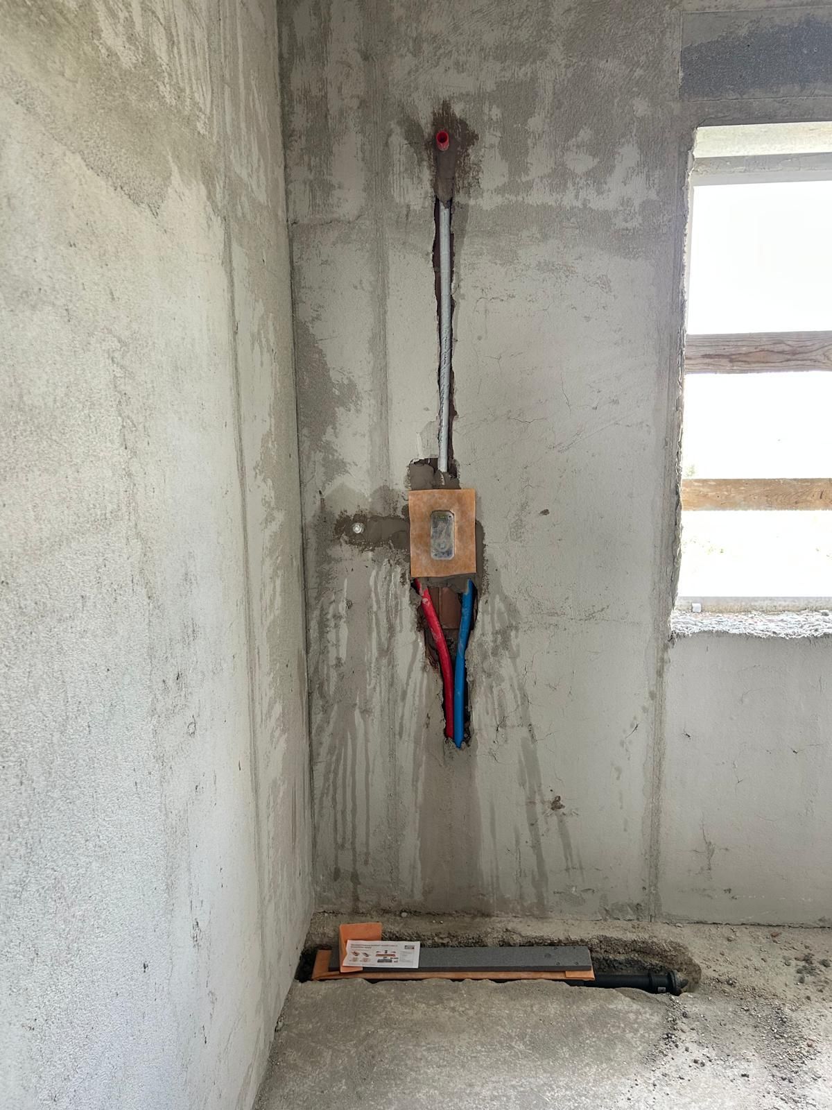 Parete in cemento armato della stanza con cavi elettrici a vista e una piccola scatola del contatore vicino al pavimento.