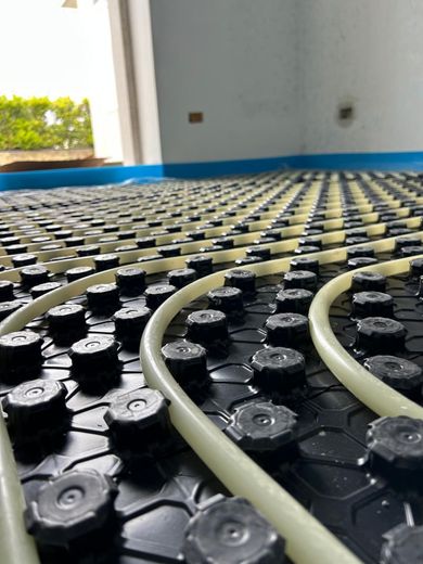 Tubi del riscaldamento a pavimento su un pannello isolante nero all'interno di una stanza in costruzione