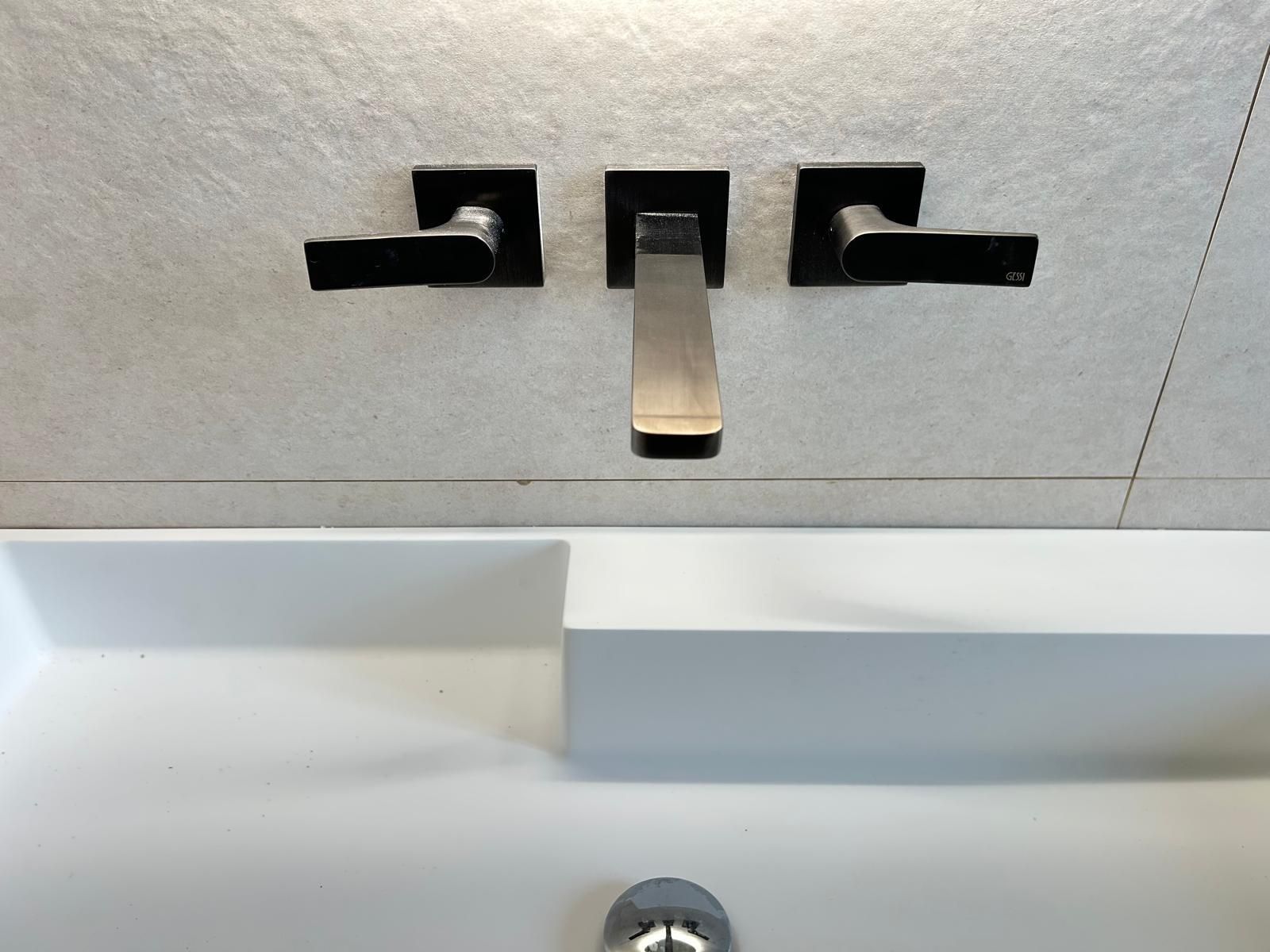 Rubinetto da bagno moderno, nero e in metallo spazzolato, sopra un lavabo bianco su piastrelle grigie.