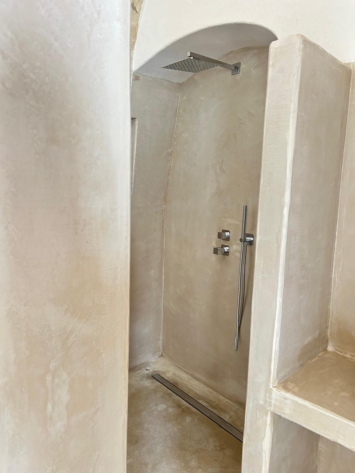 Box doccia interno stretto con pareti beige, soffione e porta in vetro in un piccolo bagno.