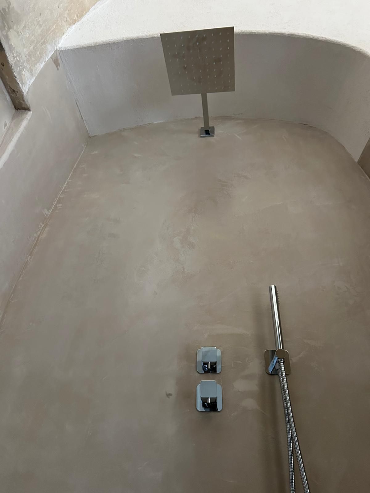 Box doccia curvo vuoto con pareti beige, scarico, due rubinetti e doccetta a mano sulla destra.