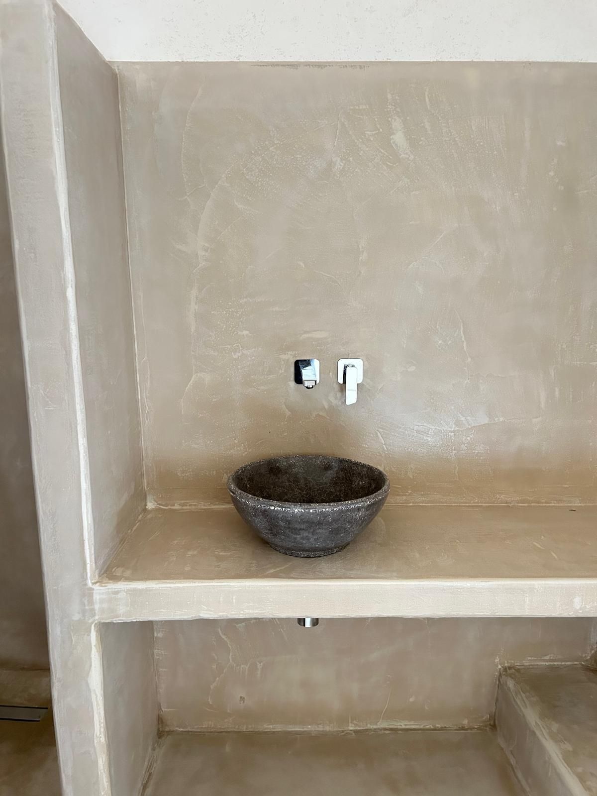 Piccola zona lavanderia non rifinita con lavabo in pietra e rubinetto a parete su un piano beige.