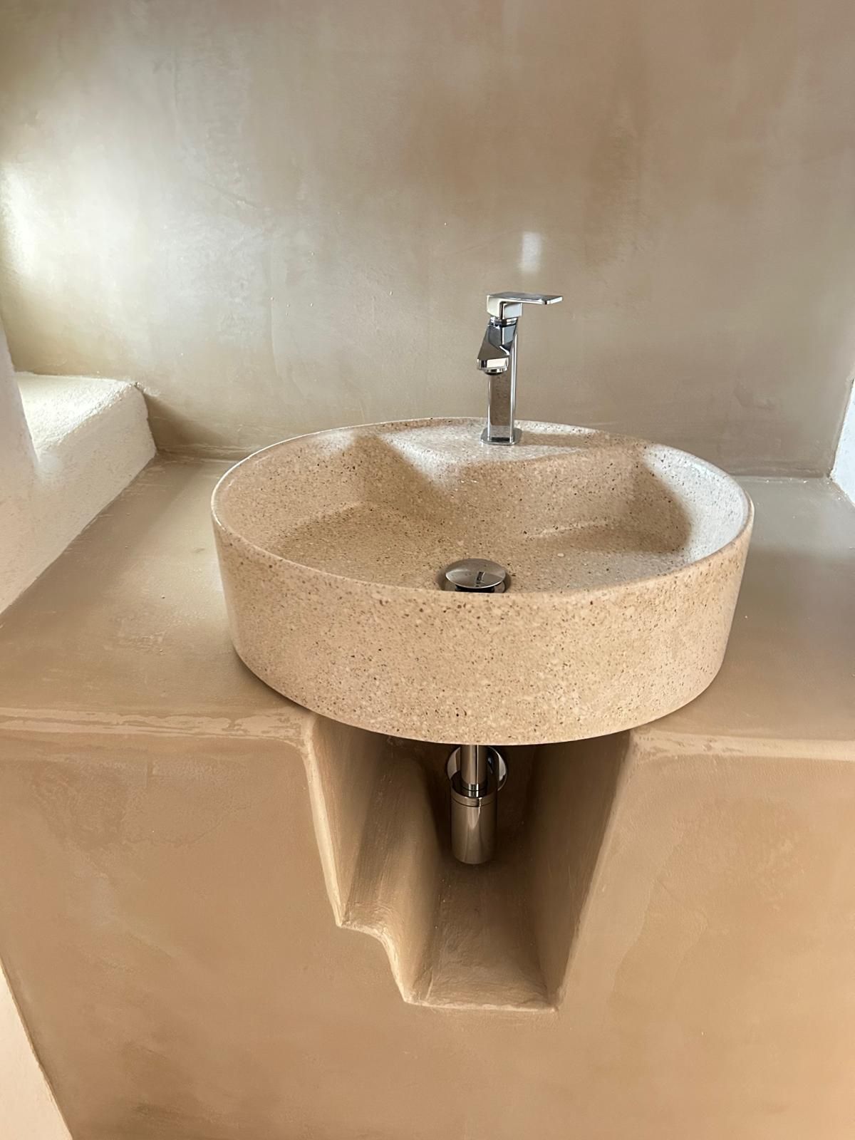 Lavabo rotondo in pietra beige con rubinetto cromato in un bagno minimalista.