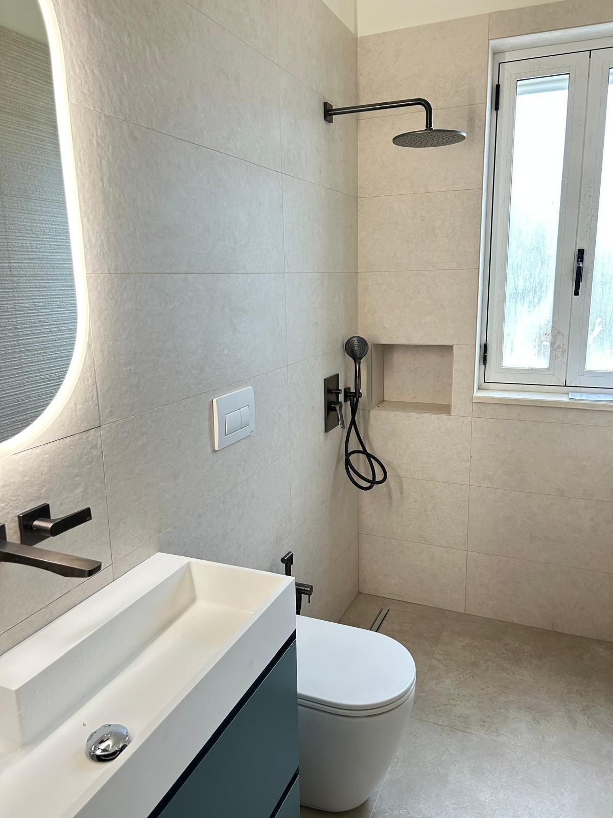 Bagno moderno color beige con lavabo, WC, doccia e finestra.