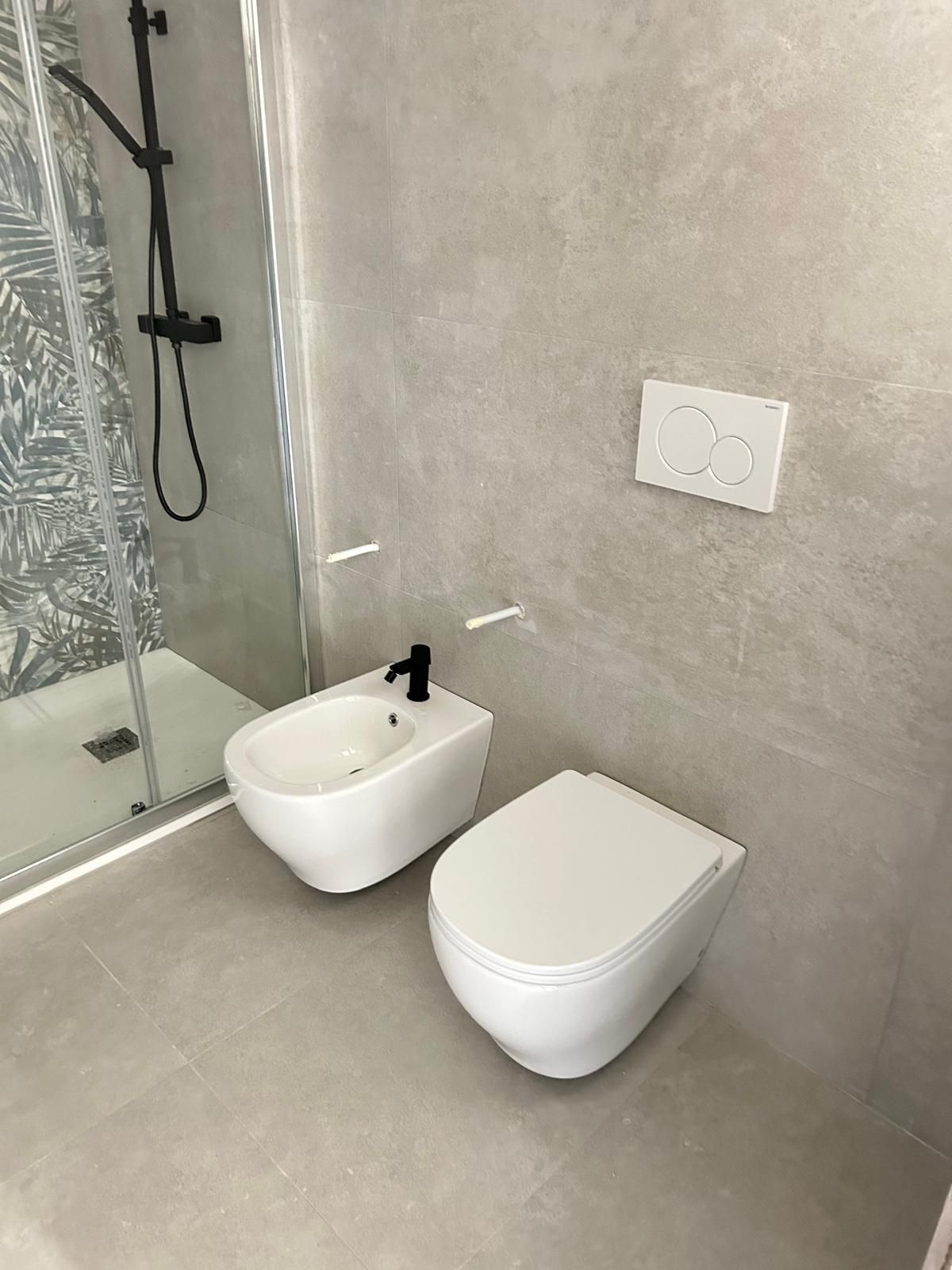 Bagno moderno con cabina doccia, WC sospeso e bidet su pavimento in piastrelle grigie.