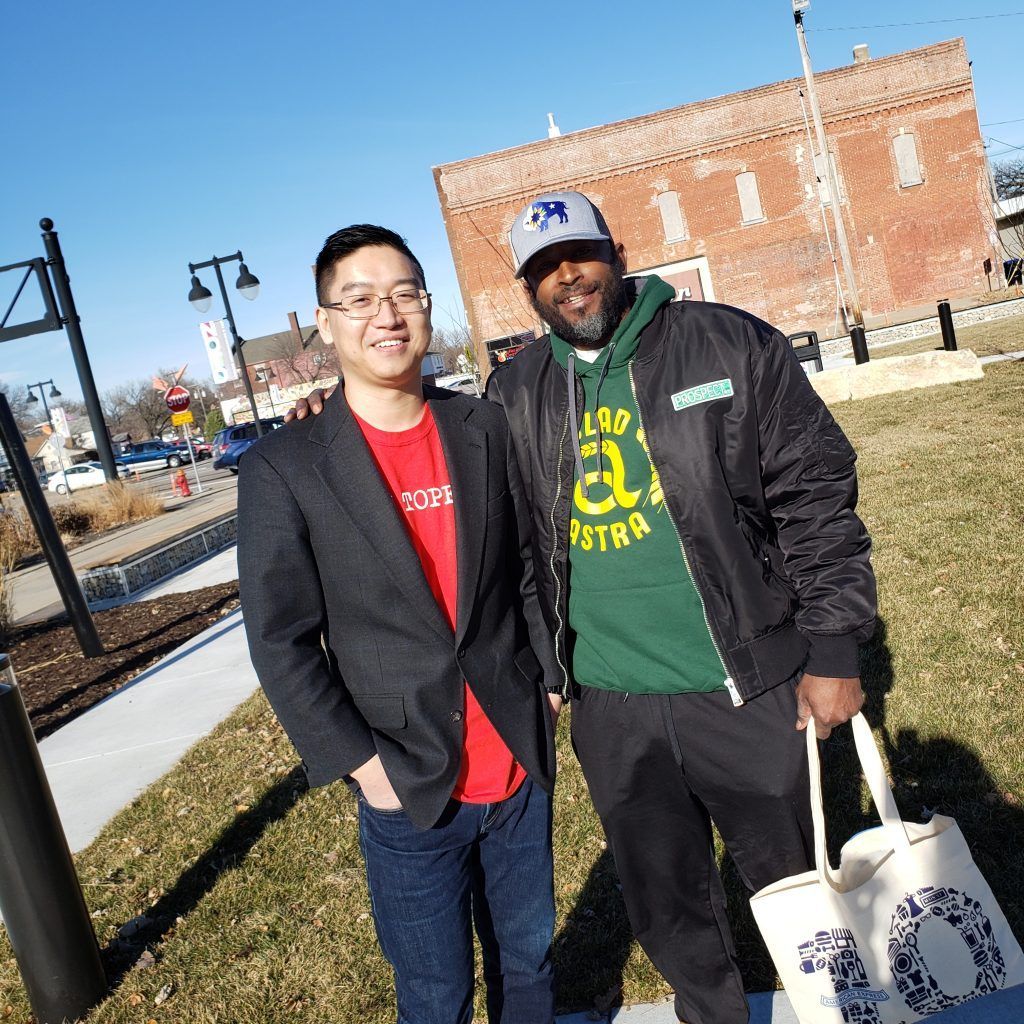 Two men are posing for a picture in front of a brick building.