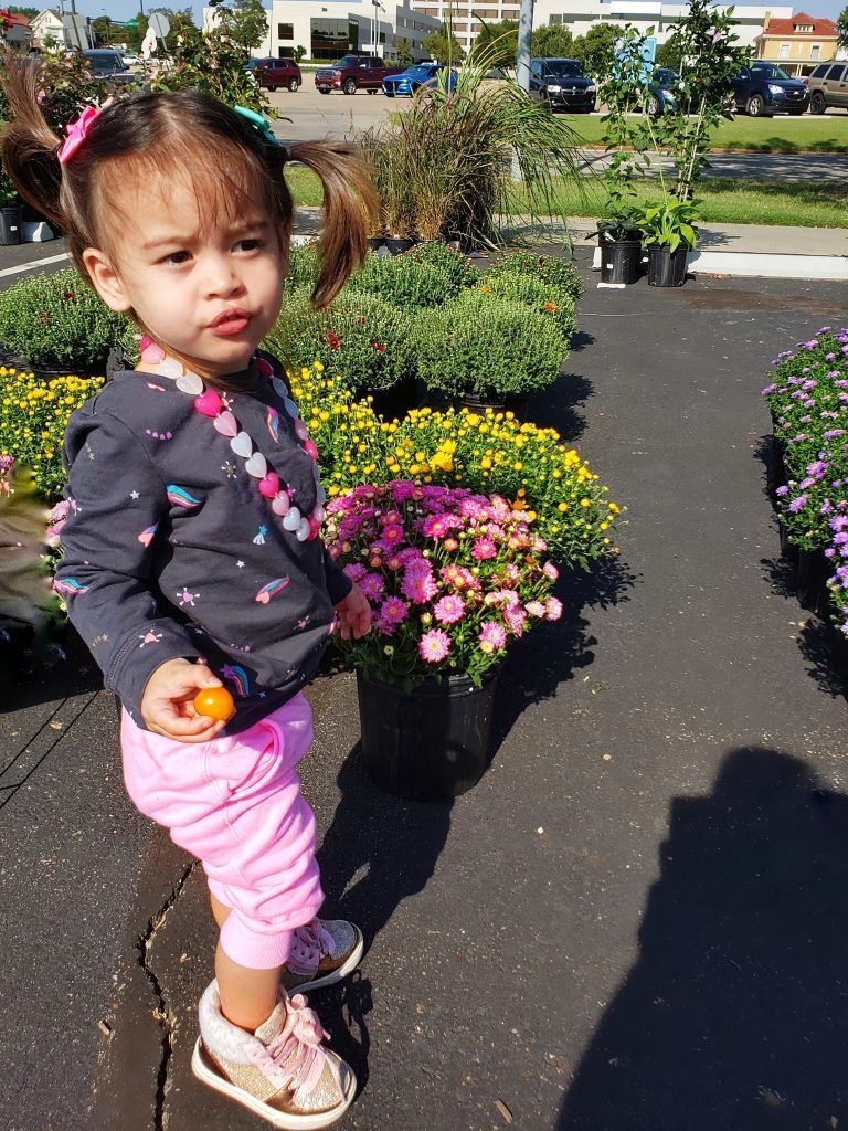 A little girl is standing in front of a bunch of potted plants.