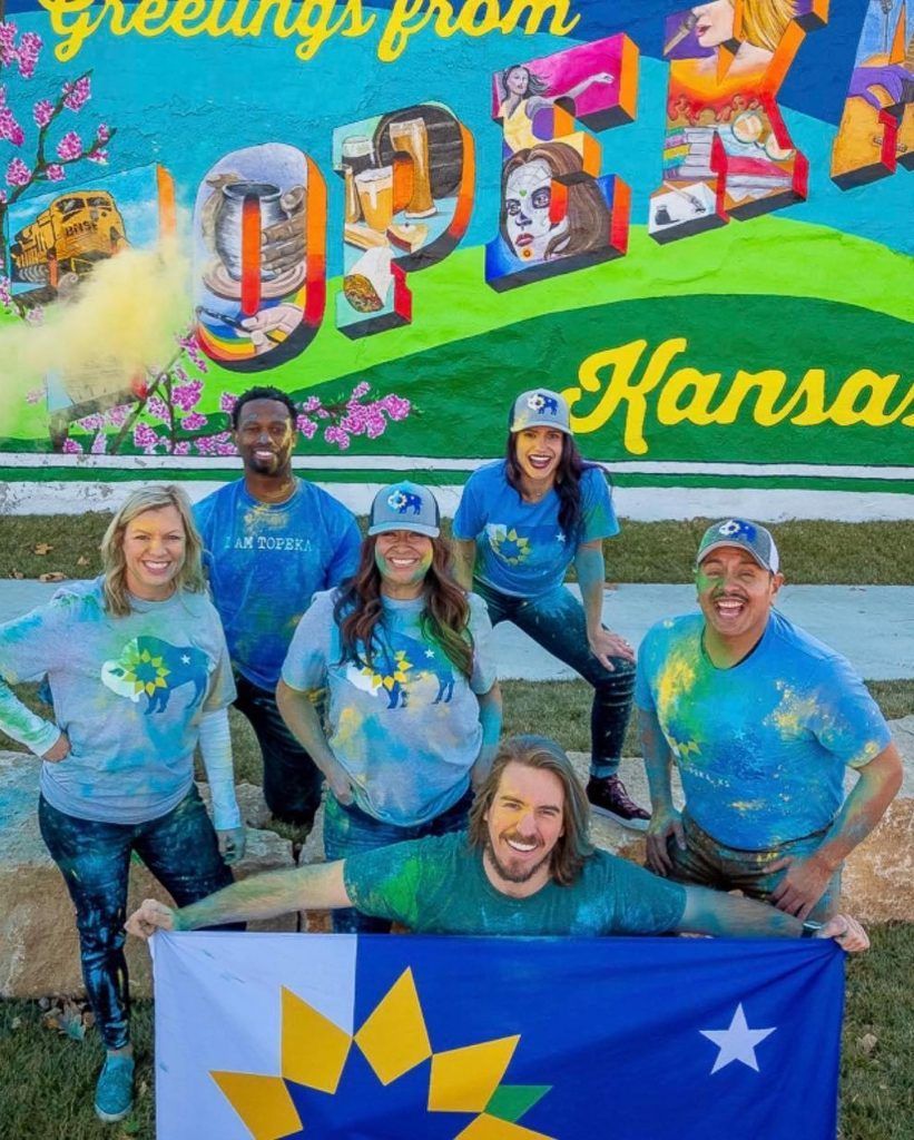 A group of people are posing for a picture in front of a sign that says greetings from kansas.