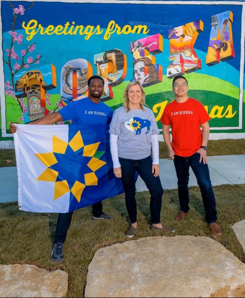 Three people standing in front of a sign that says greetings from texas