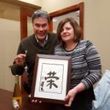A man and a woman are holding a framed picture with chinese writing on it.