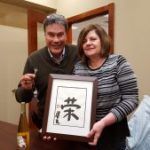 A man and a woman are holding a framed picture with chinese writing on it.