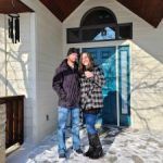 A man and a woman are standing in front of a house in the snow.