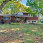 A brick house with a large lawn in front of it surrounded by trees.
