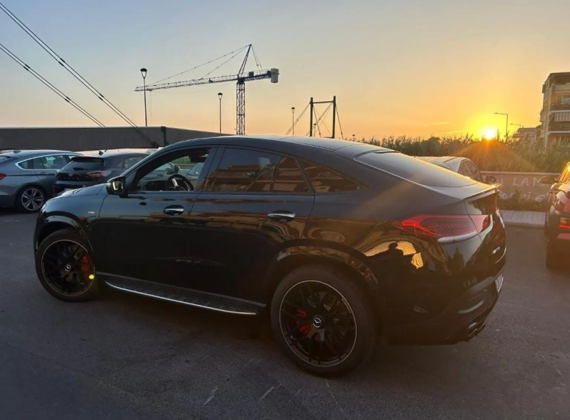 Berlina sportiva nera parcheggiata al tramonto con gru edili sullo sfondo.