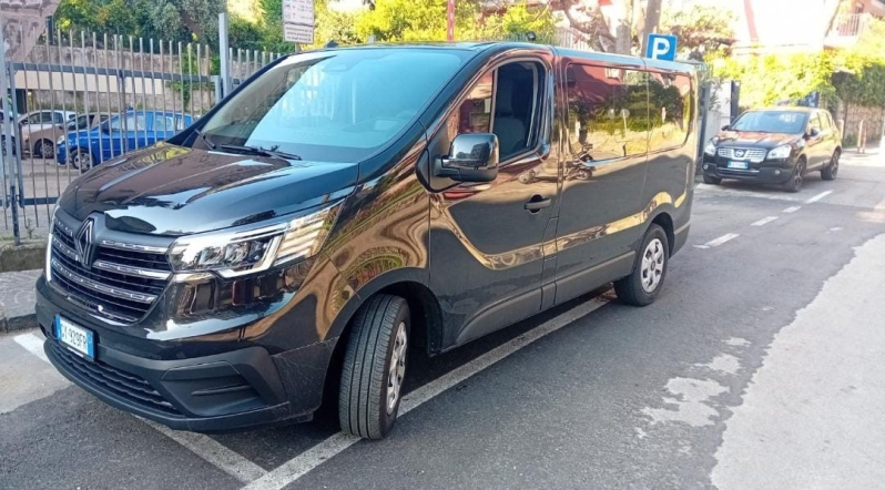 Un furgone nero parcheggiato su una strada cittadina, accanto al marciapiede, con un'altra auto dietro.
