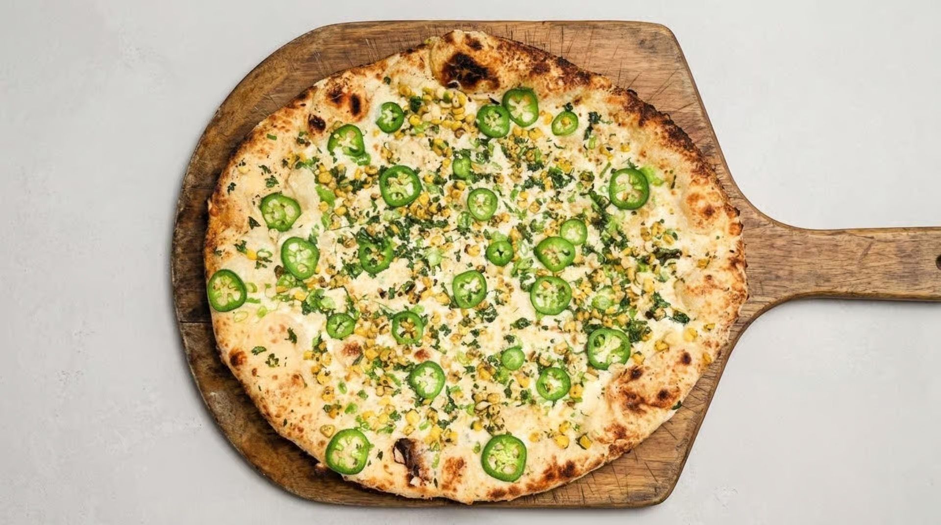 Flatbread pizza topped with sliced green peppers on a wooden paddle, viewed from above.