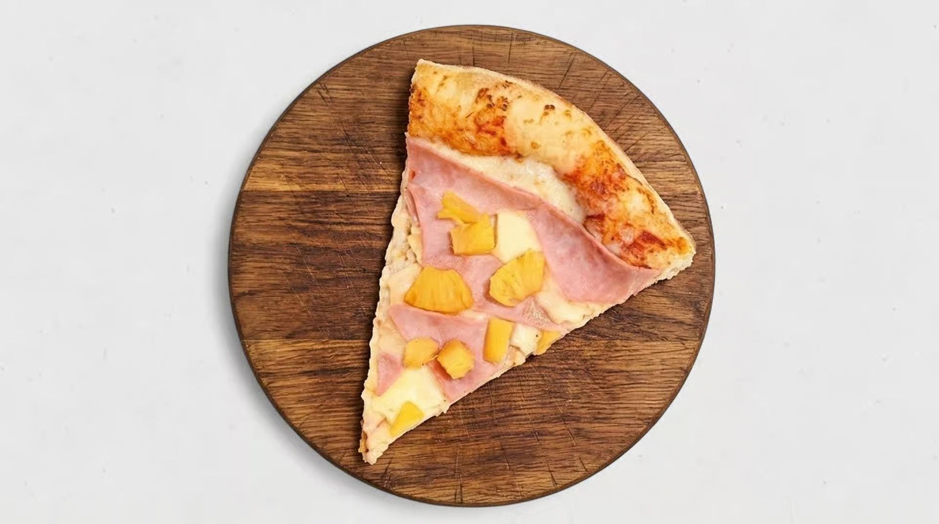 Slice of pizza with ham and pineapple on a round wooden board