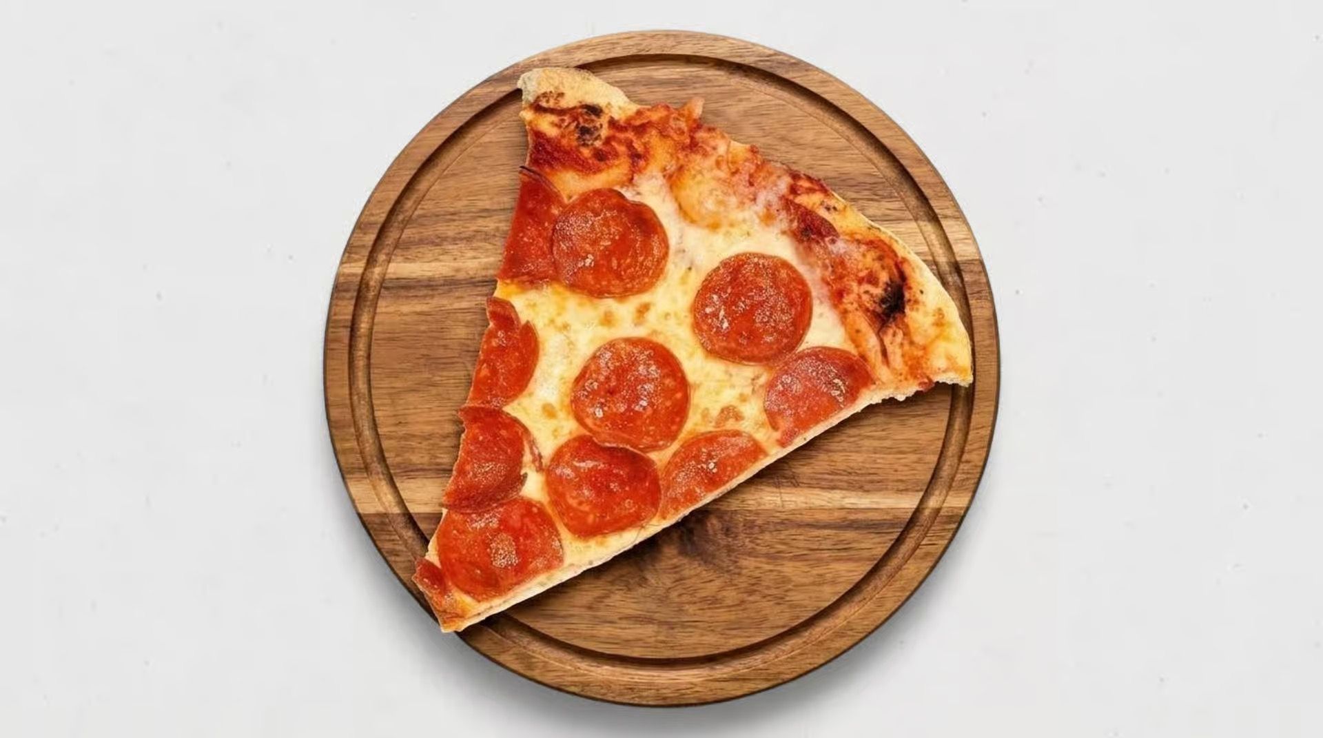 Slice of pepperoni pizza on a round wooden board over a white background