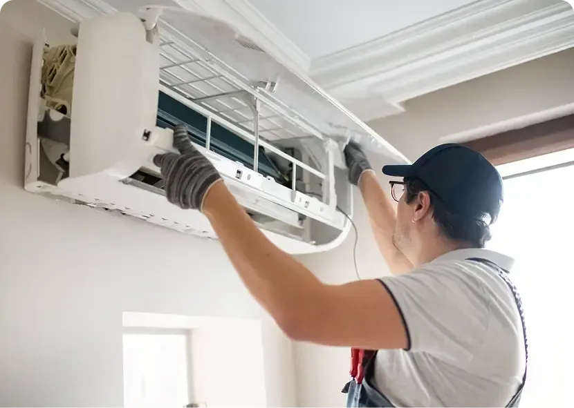 Technician cleaning a wall-mounted air conditioner with a brush and cloth