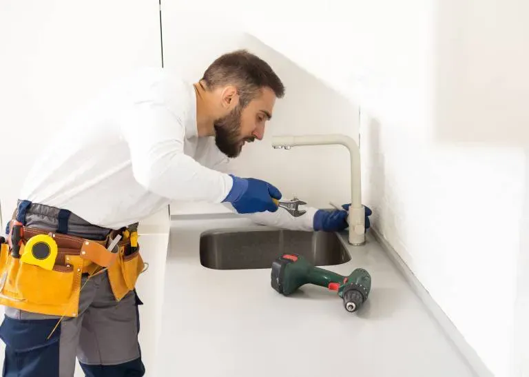 Plumber installing a sink faucet in a bright kitchen with tools on the counter