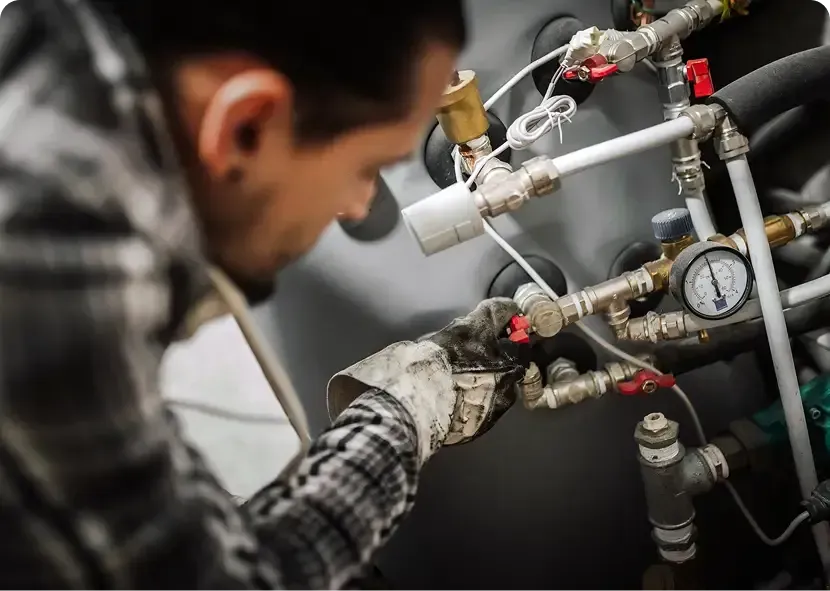 Technician inspecting industrial piping with a gauge and valves in a workshop