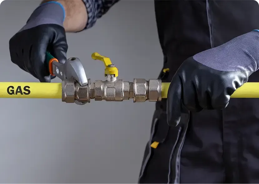 Gloved hands using a wrench to work on a yellow gas pipe valve