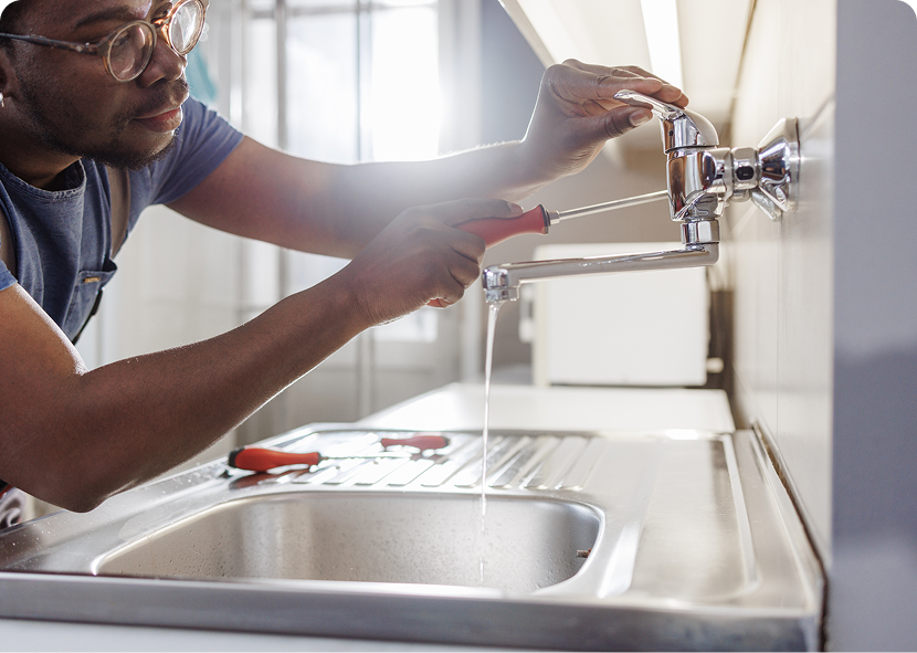 Person installing a faucet over a kitchen sink, using tools in a bright kitchen