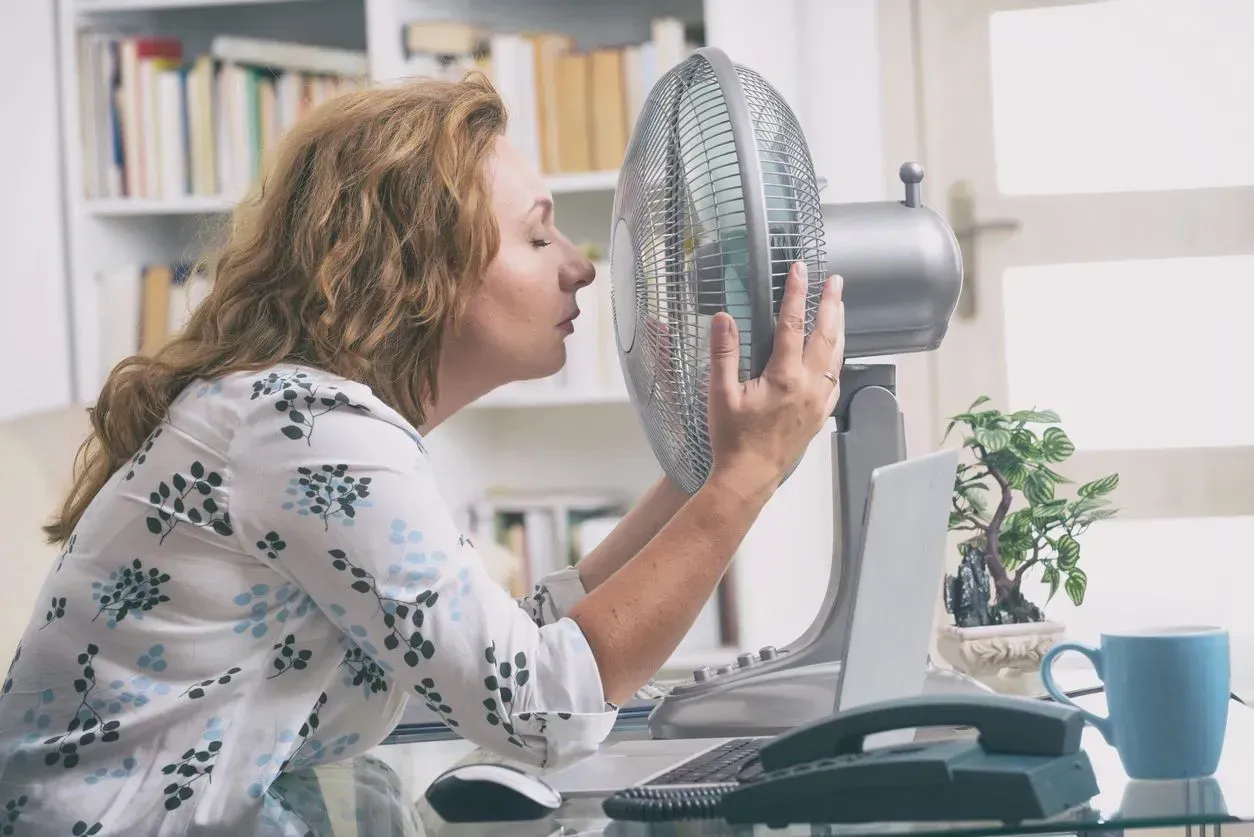 Woman blowing air into a desk fan while working at a home office desk