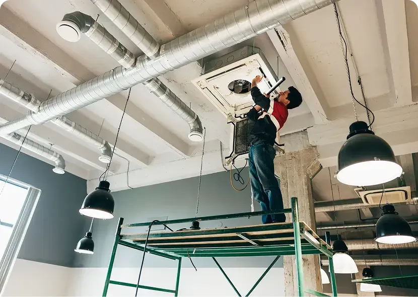 Worker on scaffold repairing a ceiling vent in a bright industrial room