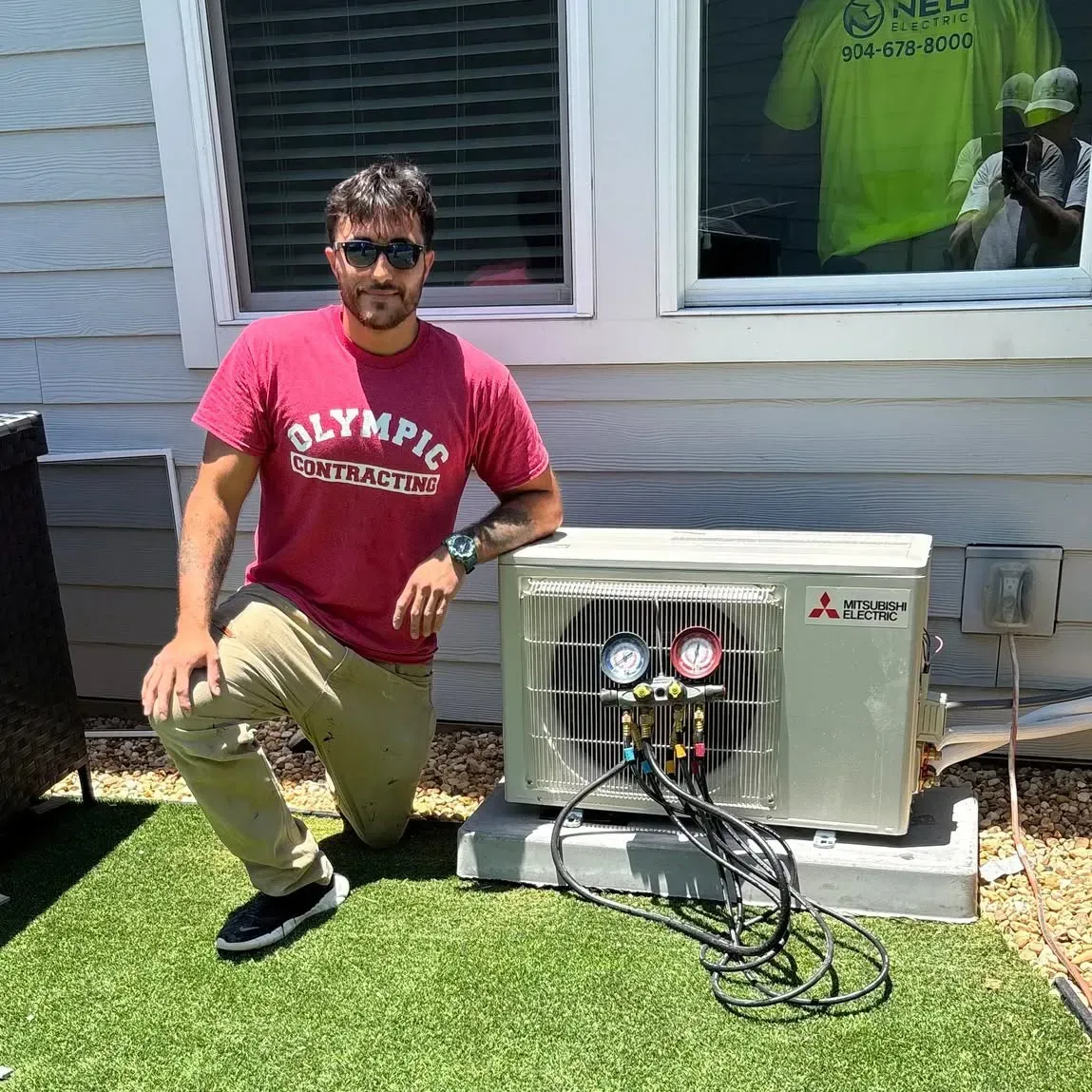 Man kneeling beside an outdoor HVAC unit next to a house, with gauges and hoses attached to the system.