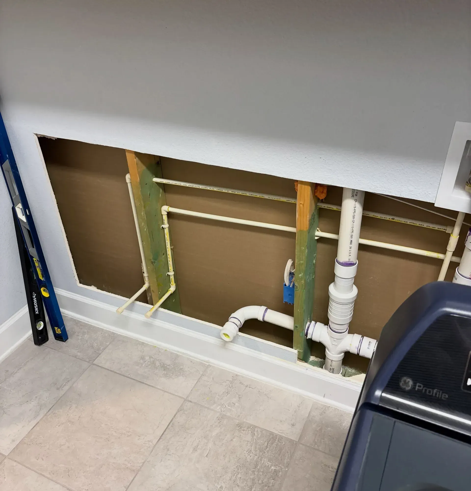 Open wall under sink with exposed plumbing and pipes in a tiled room