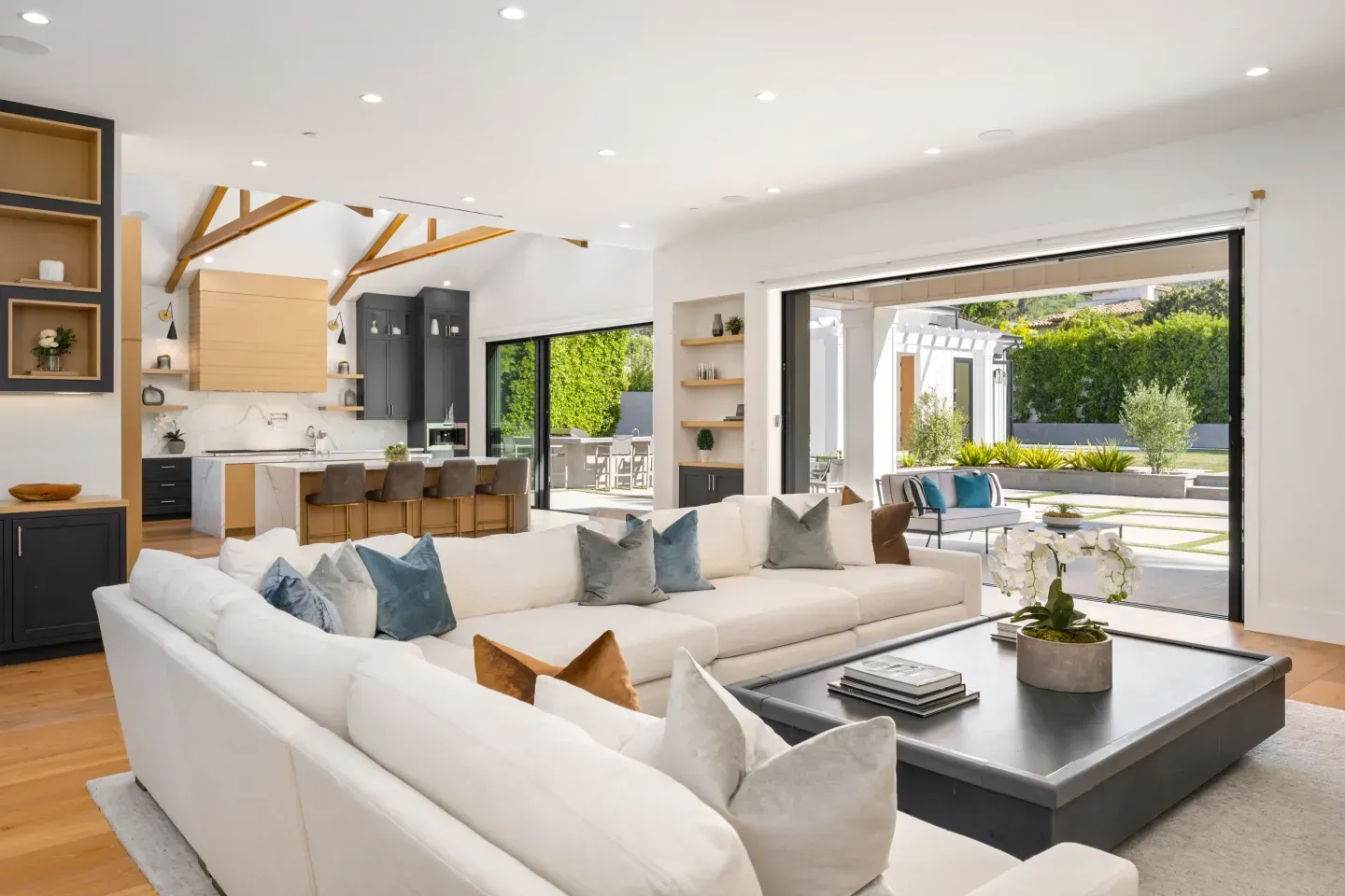 Bright modern living room with white sectional sofa, black coffee table, and open view to a sunny patio.