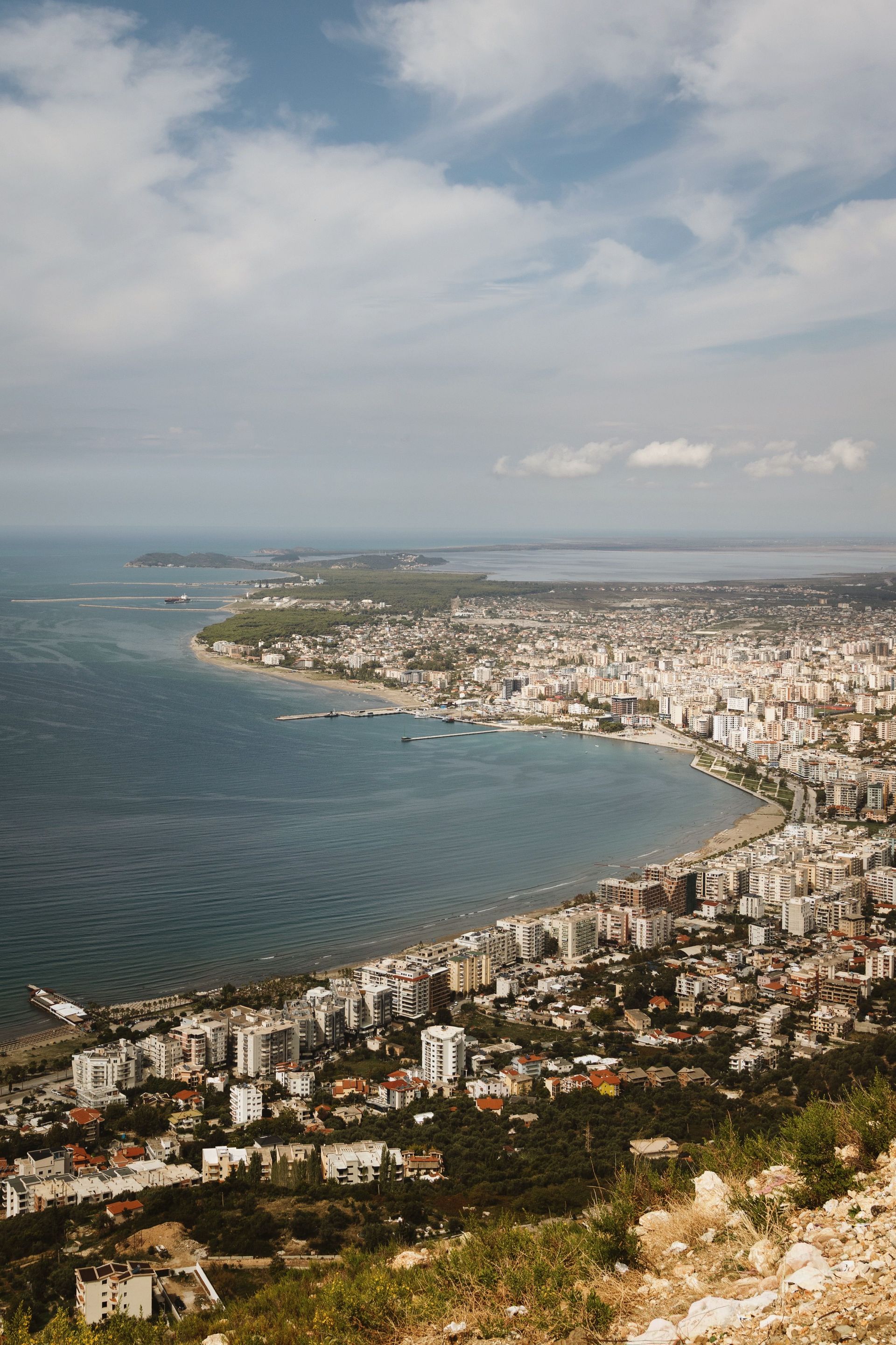 Aerial view of a coastal city curving around a blue bay under cloudy skies.