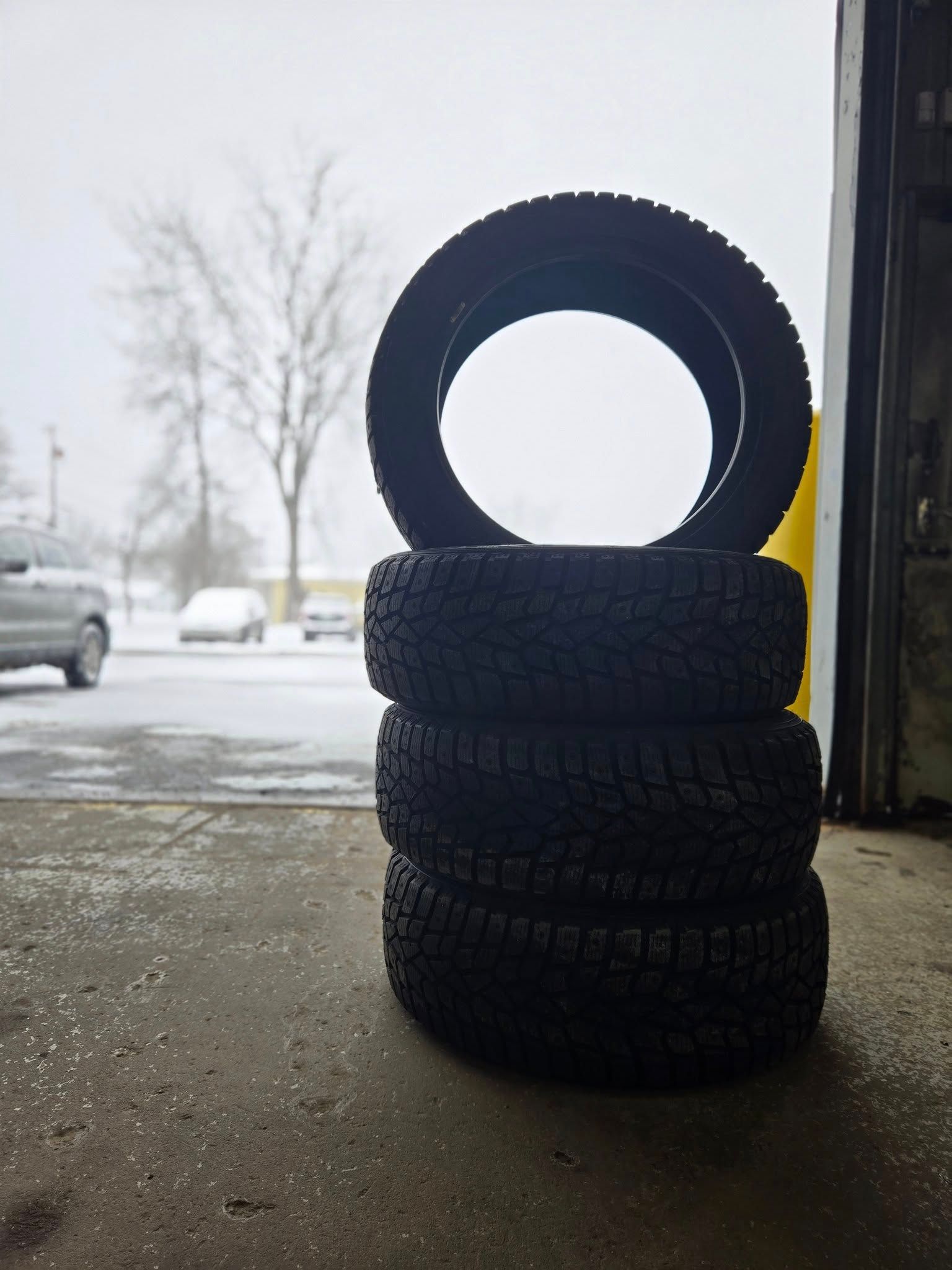 Three stacked tires with one tire standing upright on top in a garage doorway on a snowy day