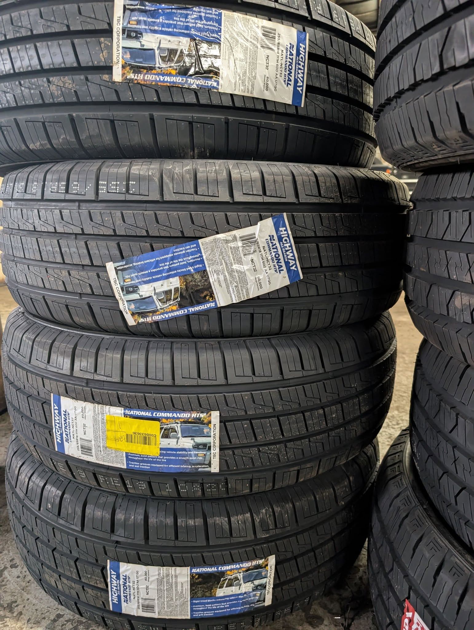 Stacked black car tires with labels in a warehouse or store aisle.