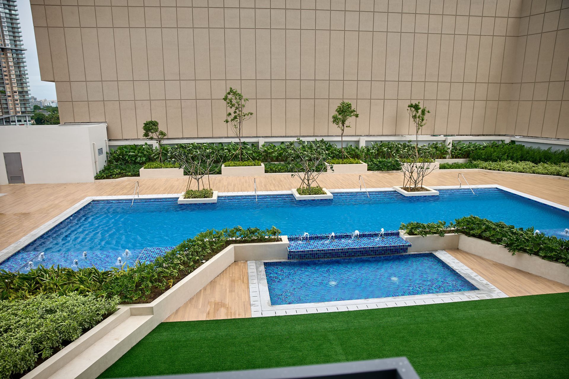 Modern outdoor pool with blue water, small bridge, and landscaped greenery in a courtyard setting