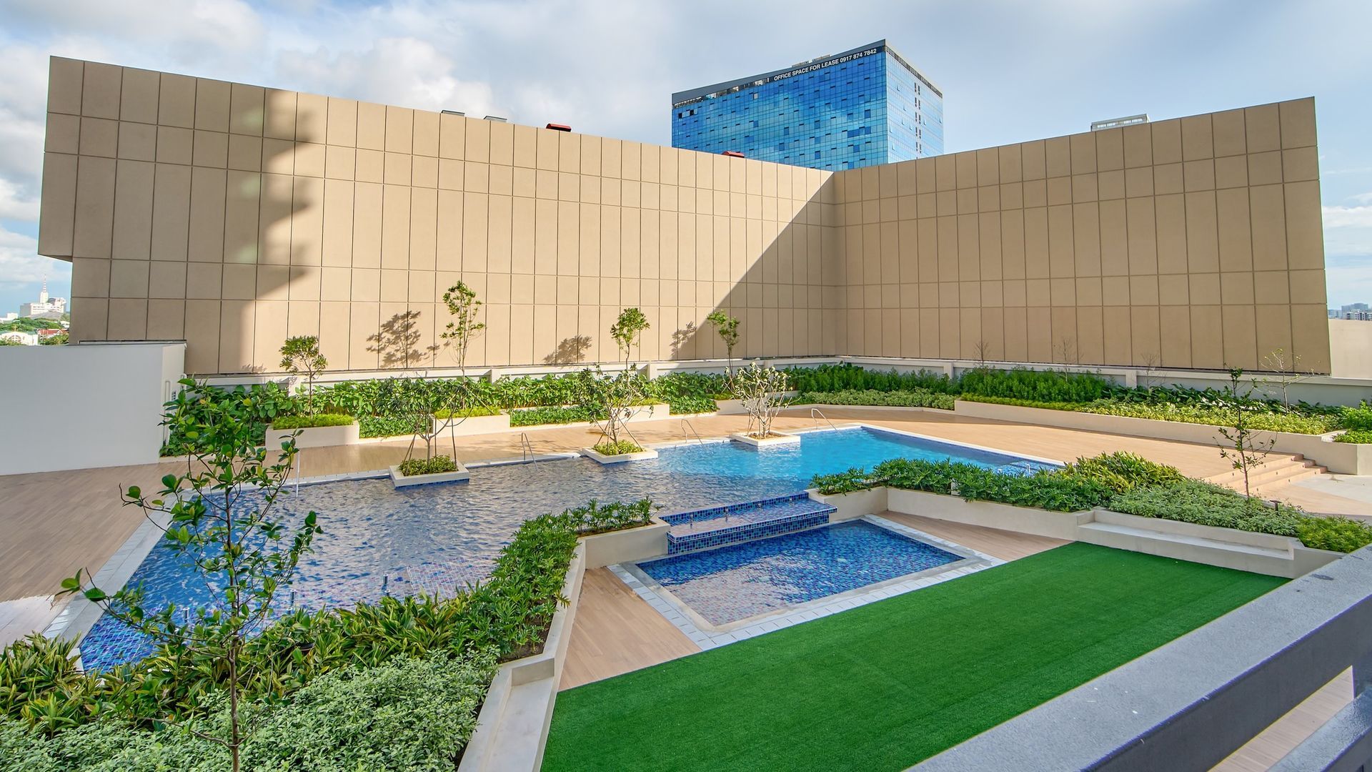 Rooftop pool area with three pools, green turf, and beige building with blue glass building in the background.
