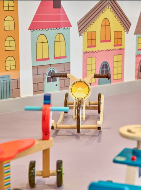 Colorful wooden toy bikes in a playful kids' area with cartoon house backdrop
