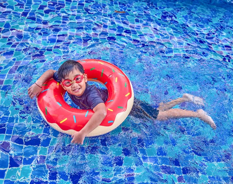 Smiling boy in donut float with goggles enjoying a sunny pool day