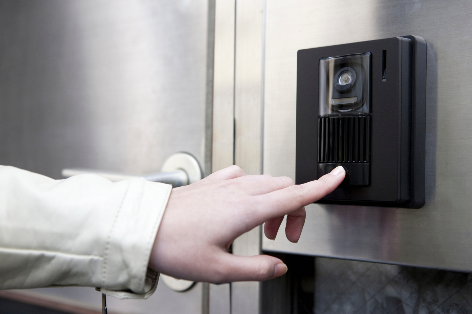 Person's hand pressing button on black security system with camera. Mounted on metal wall.
