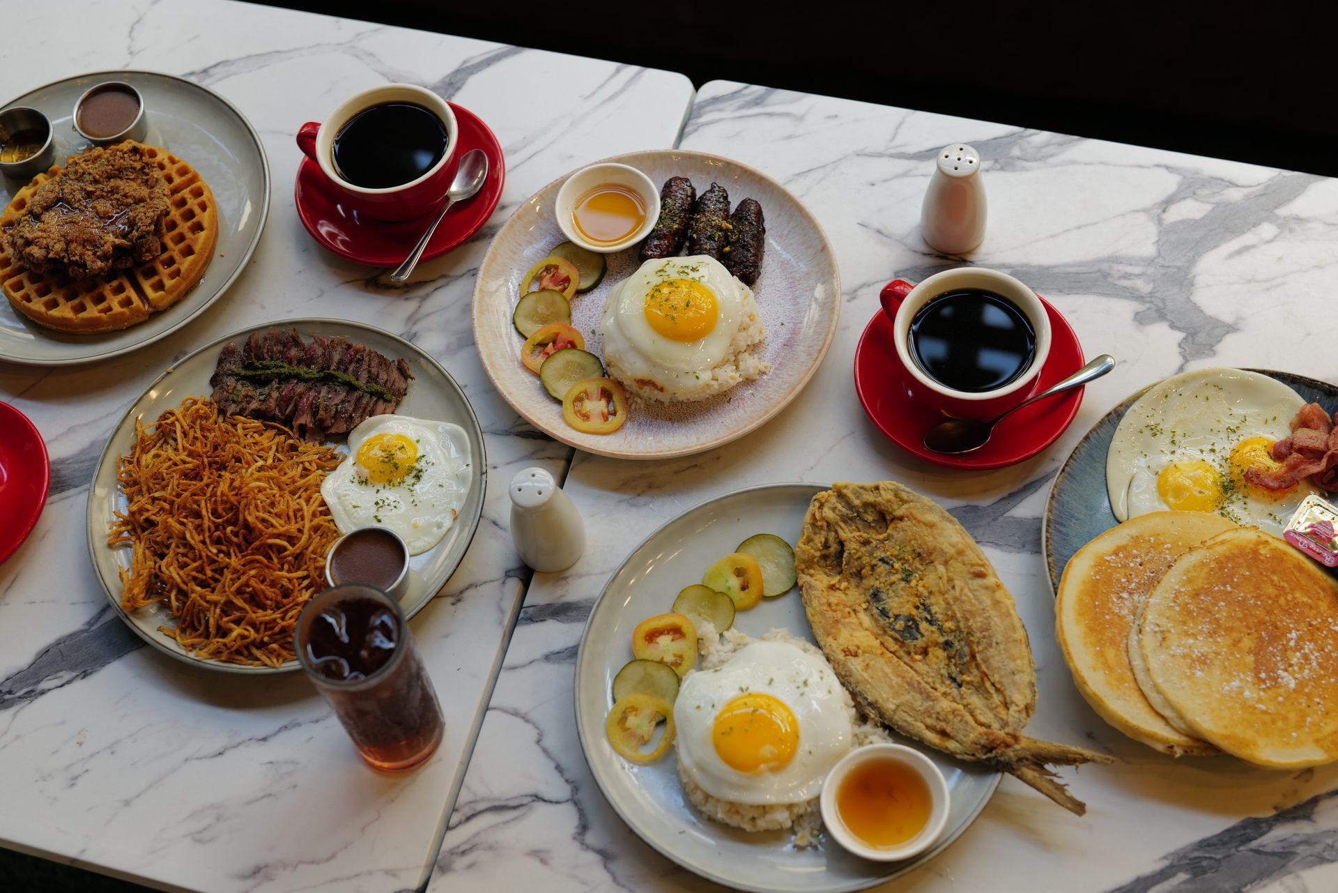 Assorted breakfast dishes and coffee cups arranged on a marble table
