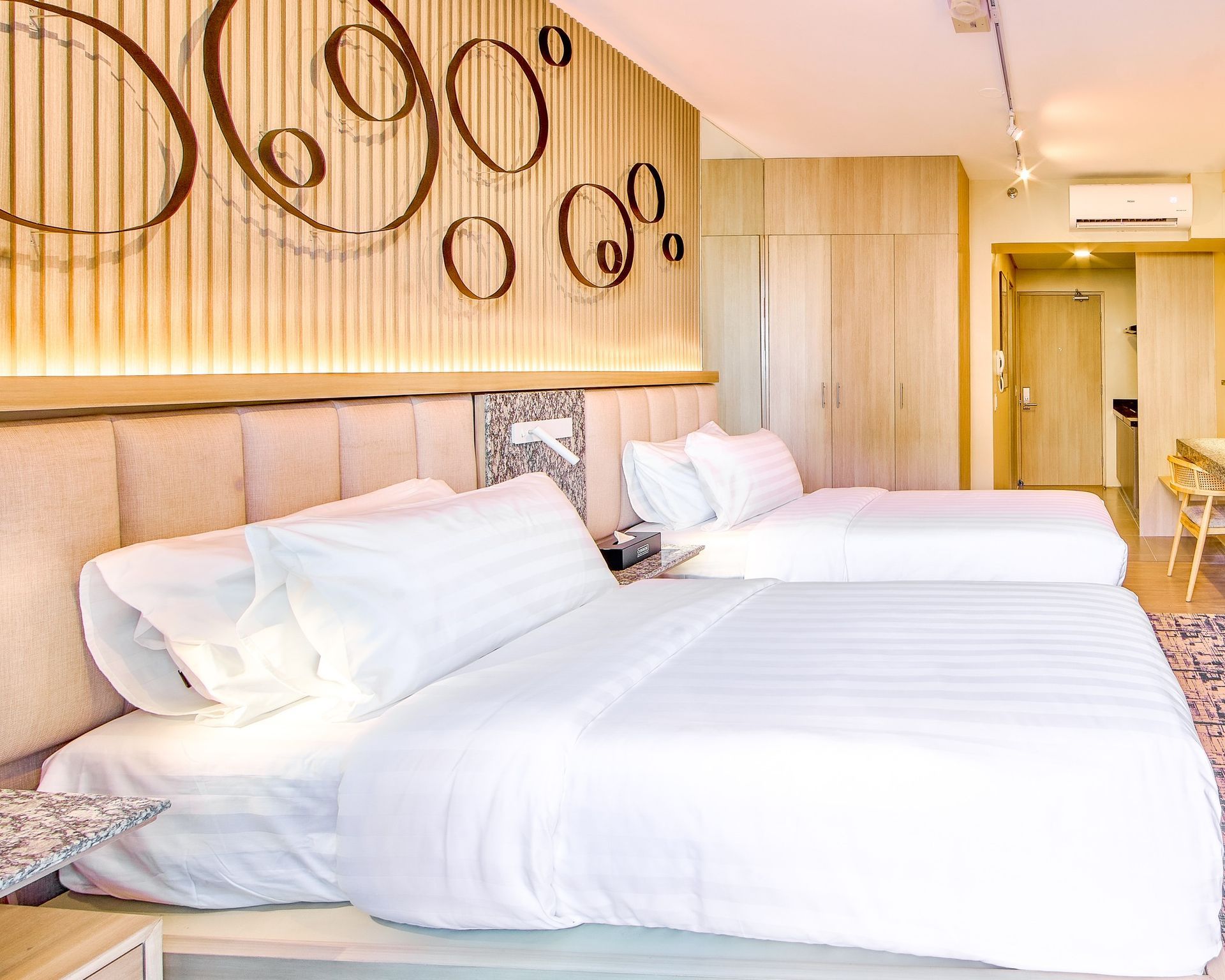 Bright modern hotel room with two white beds, wooden decor, and circular wall art
