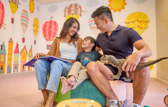 A family is sitting on a couch in a room with hot air balloons on the wall.