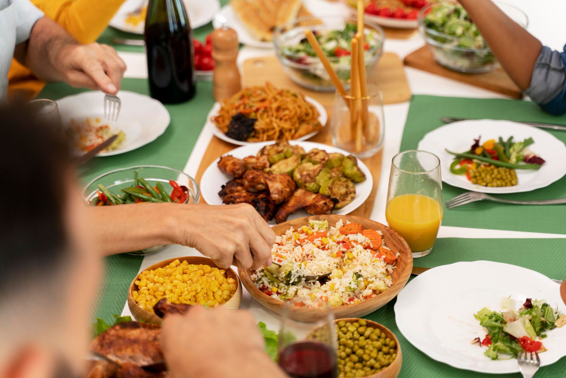 Family sharing a festive meal with rice, grilled chicken, salads, and sides