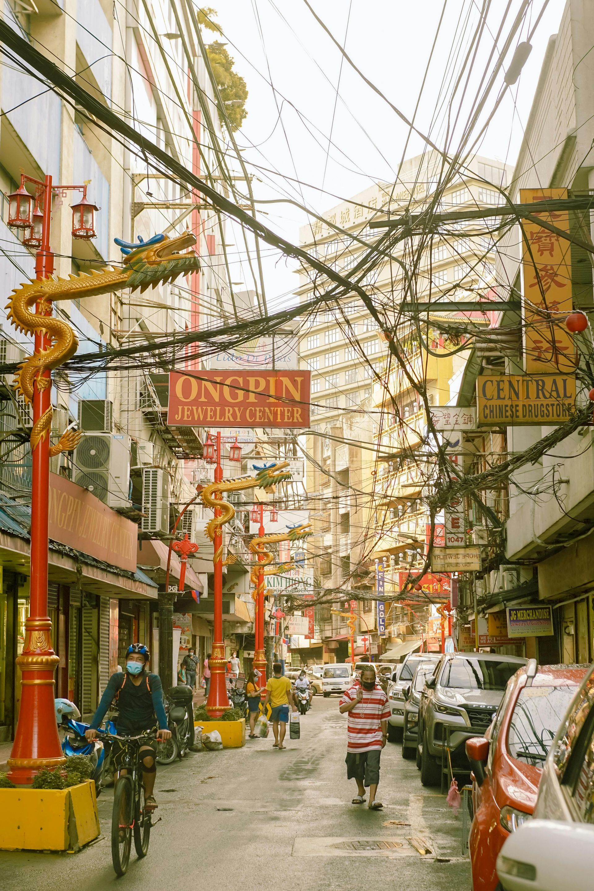 Bustling Binondo Chinatown street with golden dragon poles and tangled wires Man
