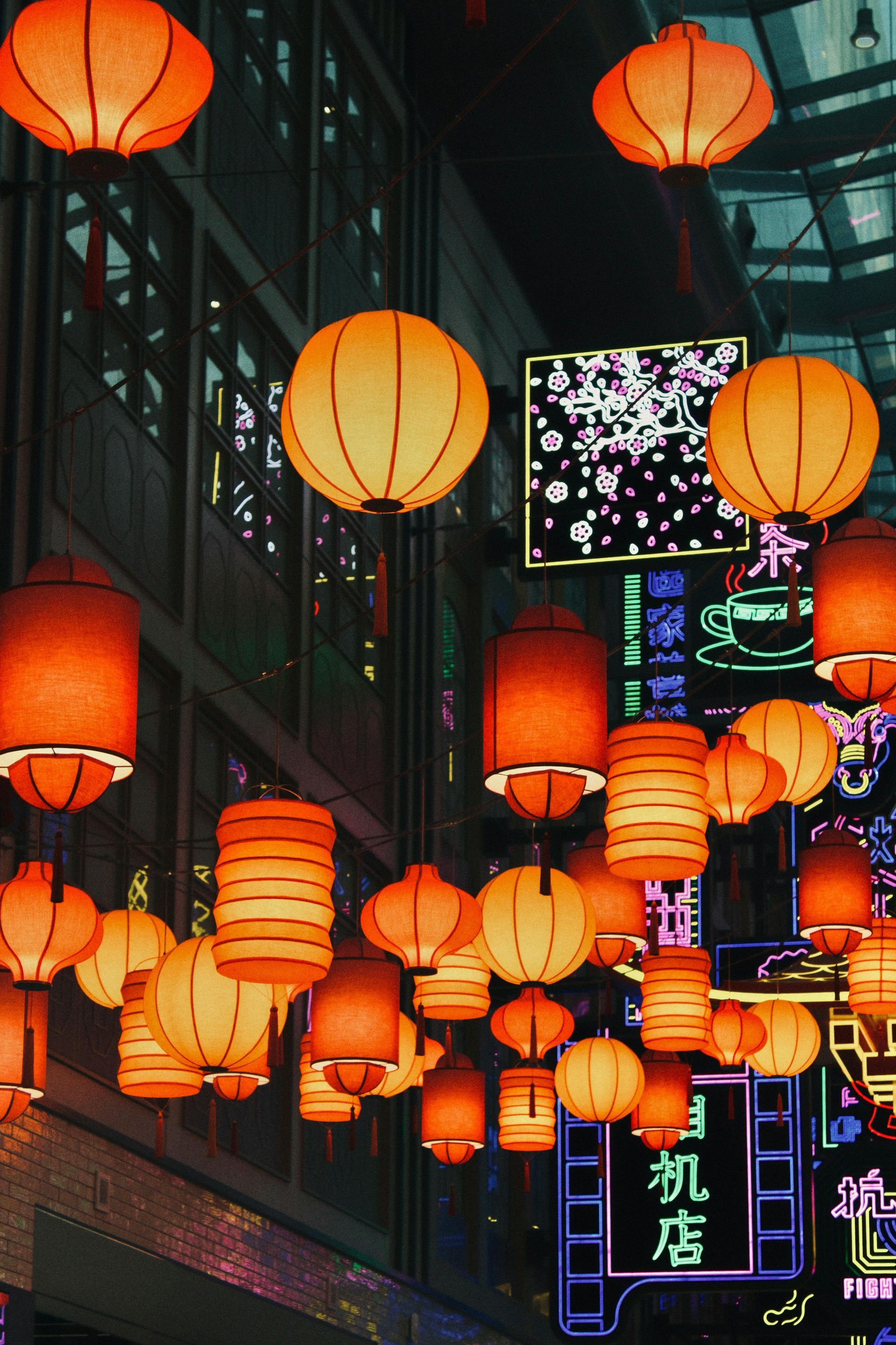 Glowing red Chinese lanterns and neon signs illuminate a vibrant night street